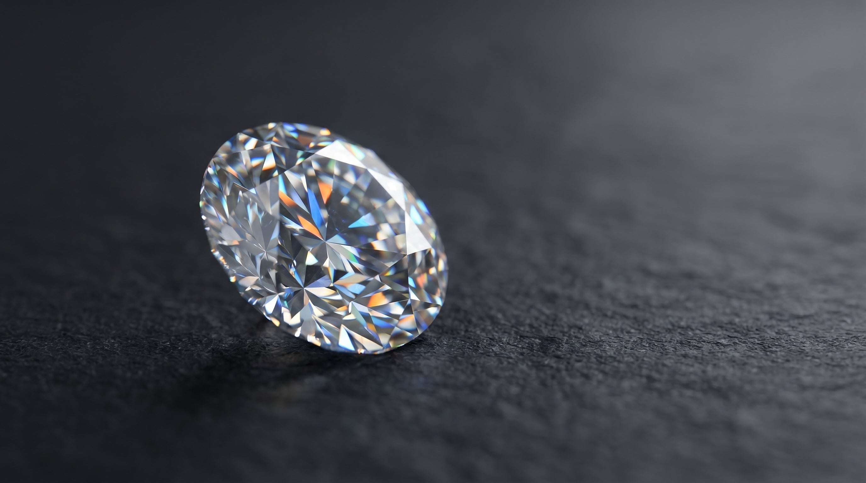 A single brilliant-cut diamond on a dark matte stone surface, showing fire and sparkle under soft directional light