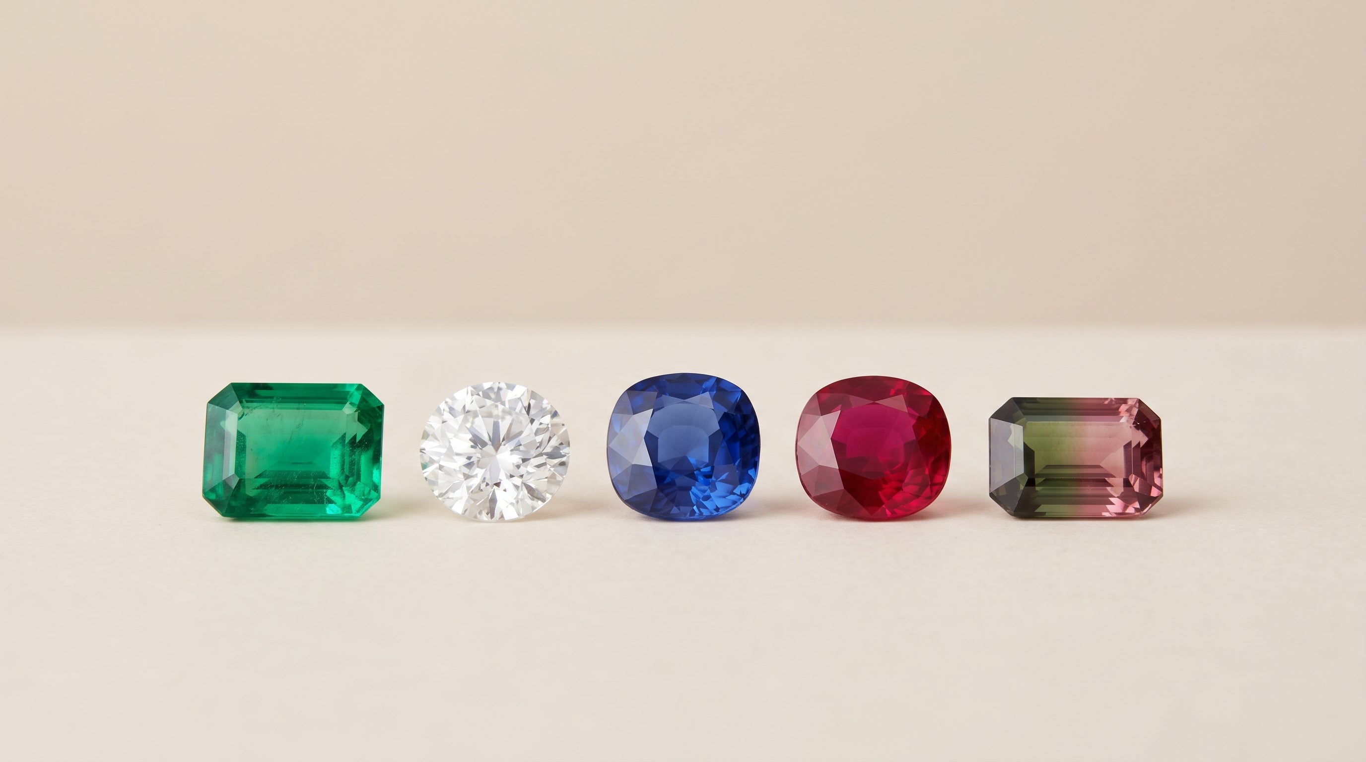 A row of faceted gemstones arranged on a pale matte surface in a clean editorial studio photograph