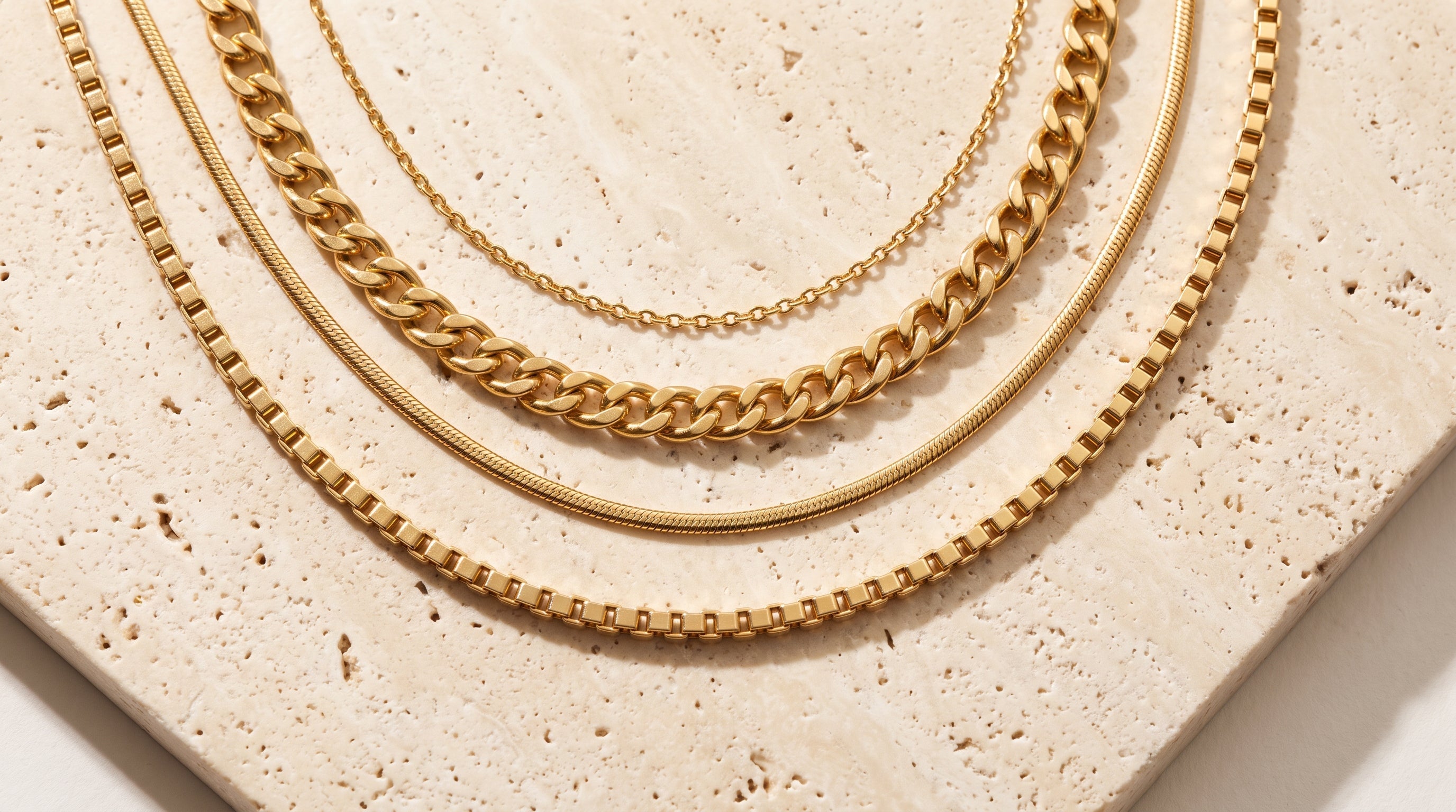 Four solid gold Italian chain styles, cable, curb, snake and box link, on travertine stone